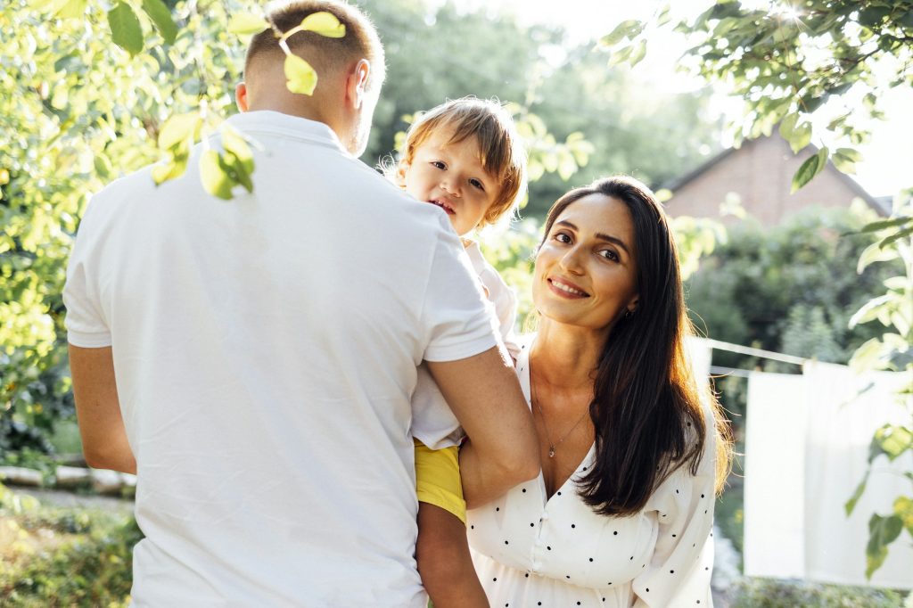 Cute family in light casual clothes in garden on terrace of their house.